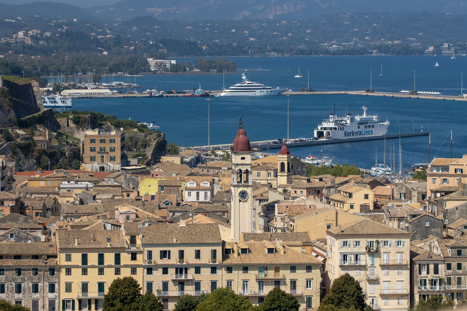 Rooftops and bell tower of Corfu Town above a harbor with ships